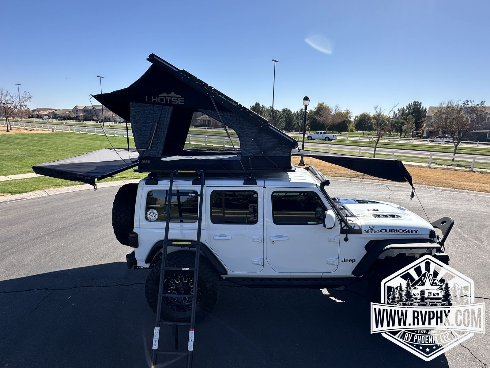 Rear-side view at camp with the rooftop tent open, awning out, and ladder in place
